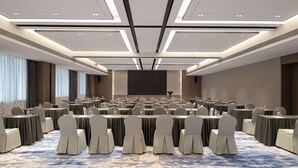 Una sala de conferencias con varias mesas y sillas, una pantalla grande y suelo alfombrado.