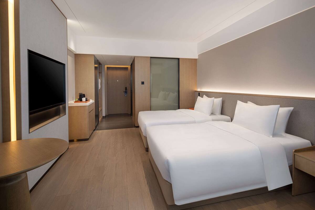 Een moderne hotelkamer met een grote flatscreen televisie, twee bedden met witte beddengoed, een houten vloer en een klein tafeltje met een koffiezetapparaat.