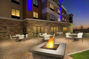 An outdoor patio area with multiple tables and chairs, a central fire feature, and a building with stone facade and windows. - Holiday Inn Express & Suites Waco South by IHG (Waco)