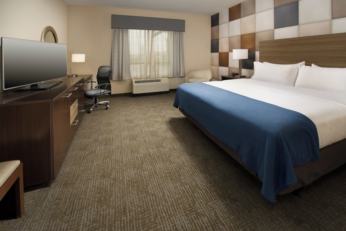 A hotel room with a bed, a desk with a TV, a chair, a lamp, and a window with curtains.