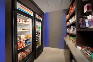 A hotel corridor with refrigerated display cases filled with food items and shelves stocked with toiletries and personal care products.