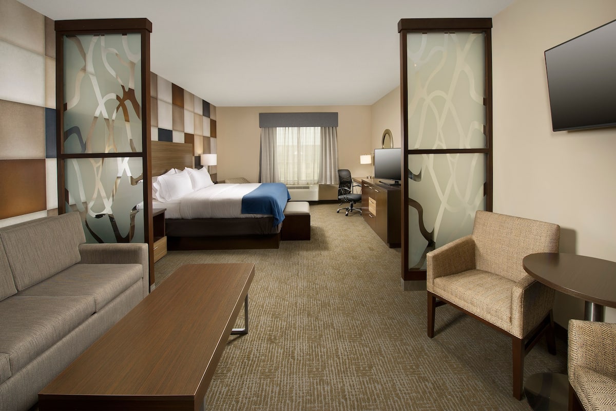 A hotel room with a bed, sofa, armchair, desk, and TV.