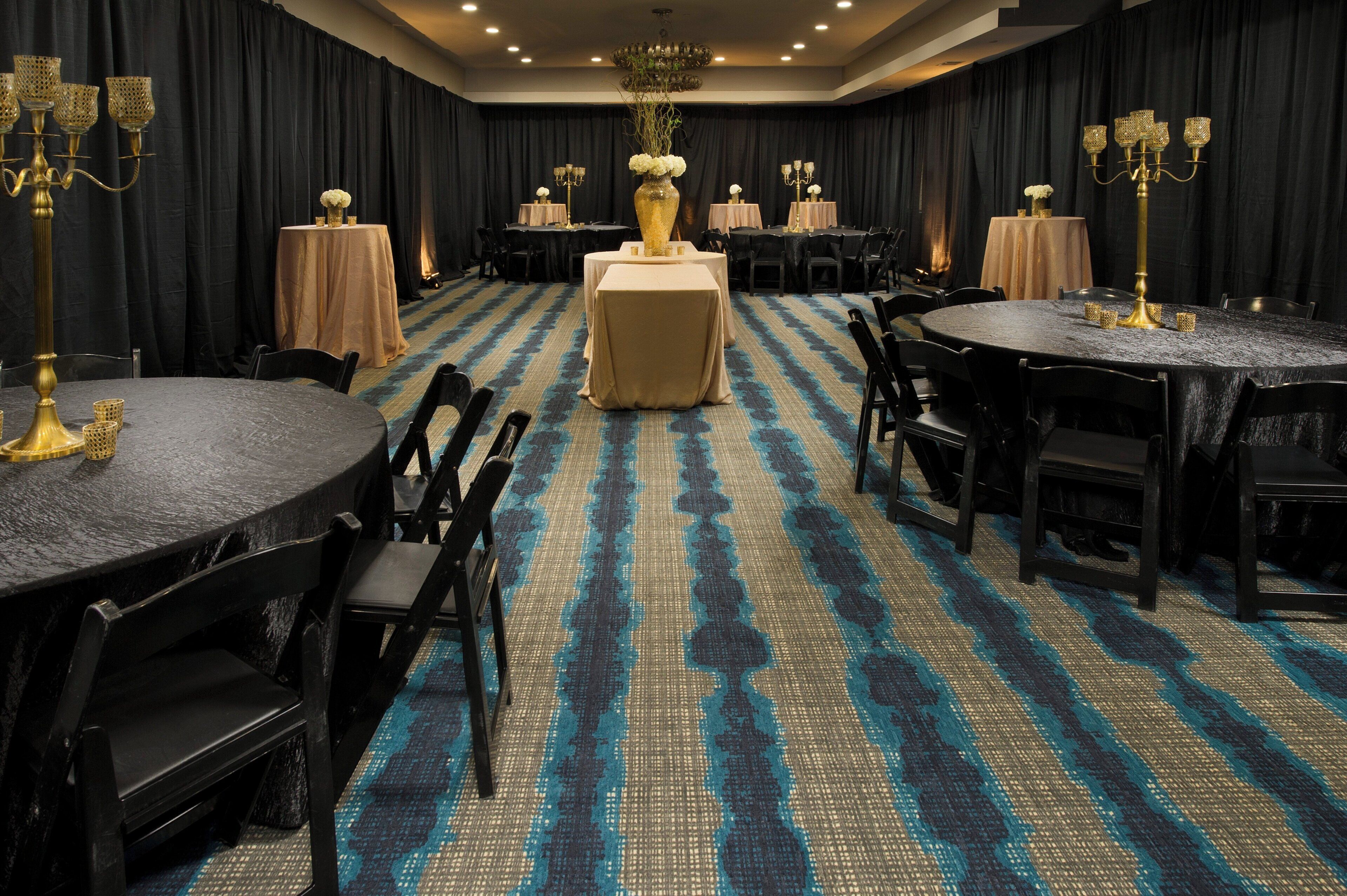 Een hotelconferentiezaal met ronde tafels, zwarte stoelen en een kamerbreed tapijt met dessin.