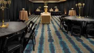 Een hotelconferentiezaal met ronde tafels, zwarte stoelen en een kamerbreed tapijt met dessin.