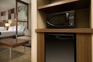 A hotel room with a bed, a sofa, a coffee table, a microwave, and a dishwasher.