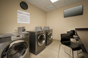 A guest laundry area with two washing machines, a clock, and a flat-screen TV. - Holiday Inn Express & Suites Waco South by IHG (Waco)