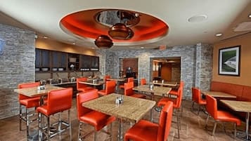 A restaurant with red chairs and tables, stone walls, and a modern ceiling design.