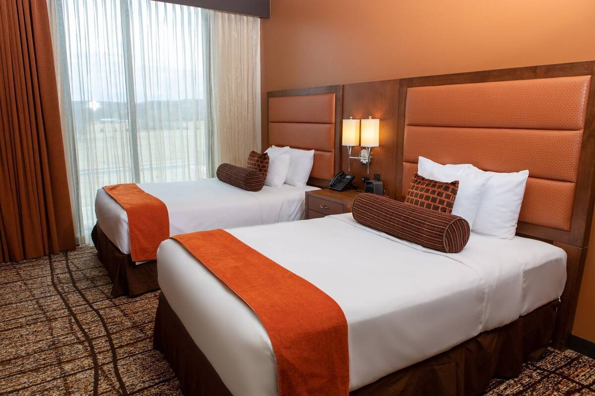 Two double beds with matching headboards, a bedside table with a phone, and a window with sheer curtains.