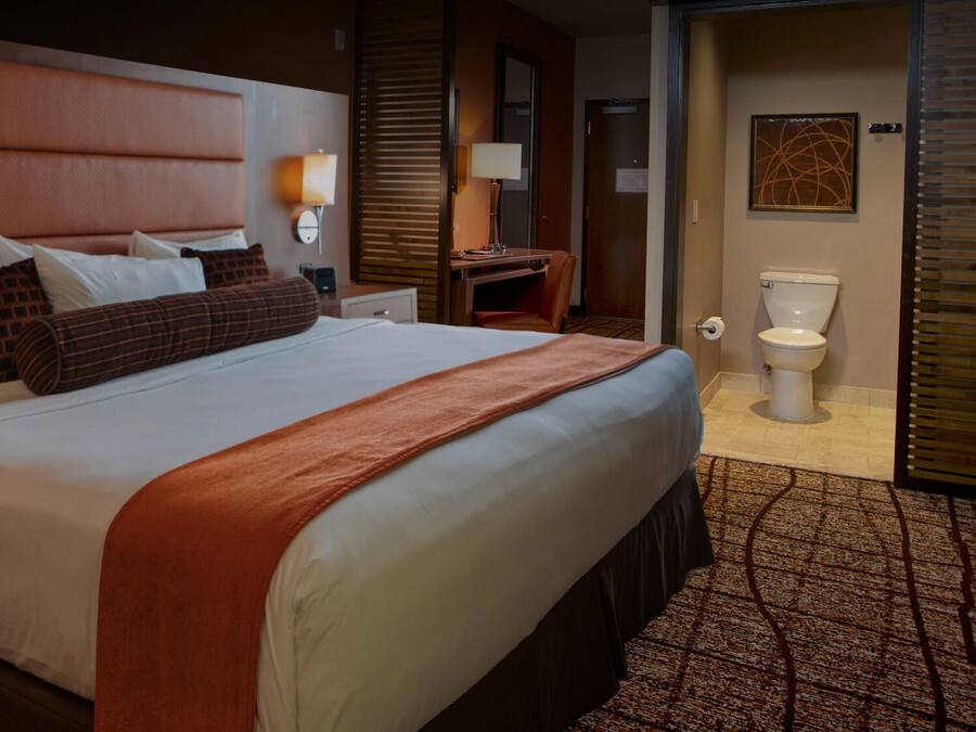 A hotel room with a large bed, bedside tables, a desk, a chair, a bathroom with a toilet, sink, and mirror.