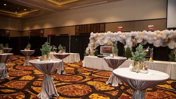 A banquet hall with round tables, floral centerpieces, and a patterned carpet.