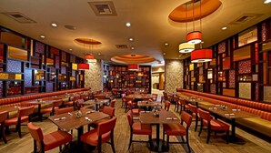 Un restaurante espacioso con varias áreas de comedor, incluidas cabinas y mesas, y un ambiente cálido y acogedor con pisos de madera y paneles decorativos.