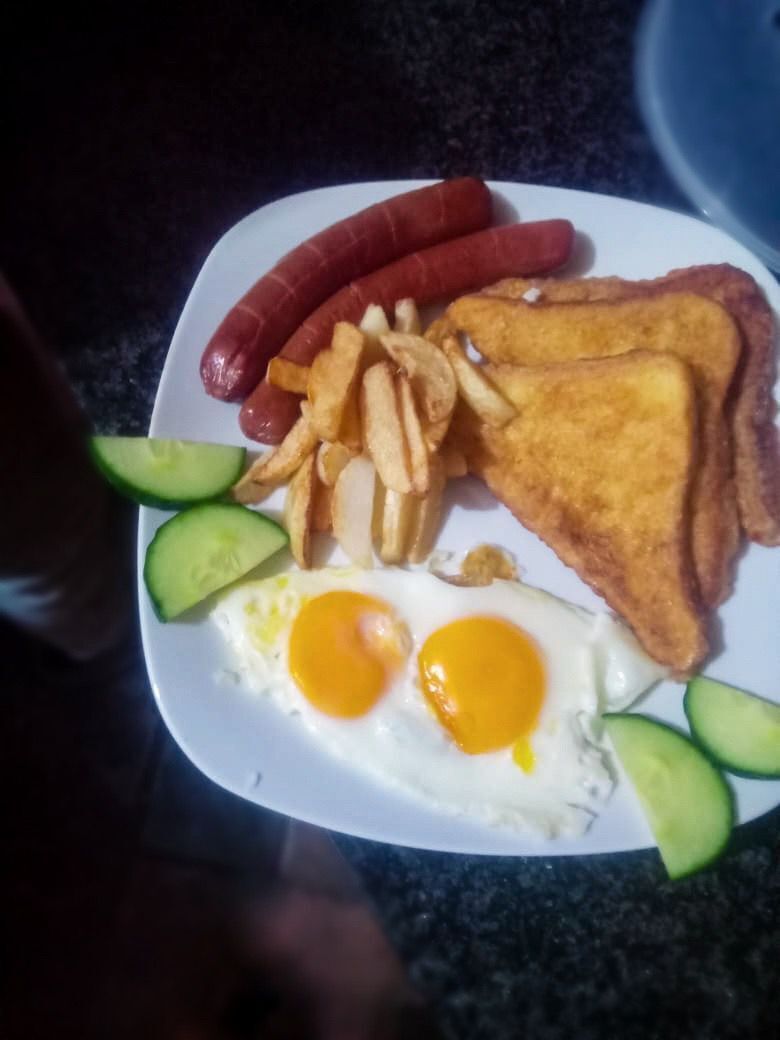 A plate with food items including sausages, fries, toast, eggs, and cucumber slices.