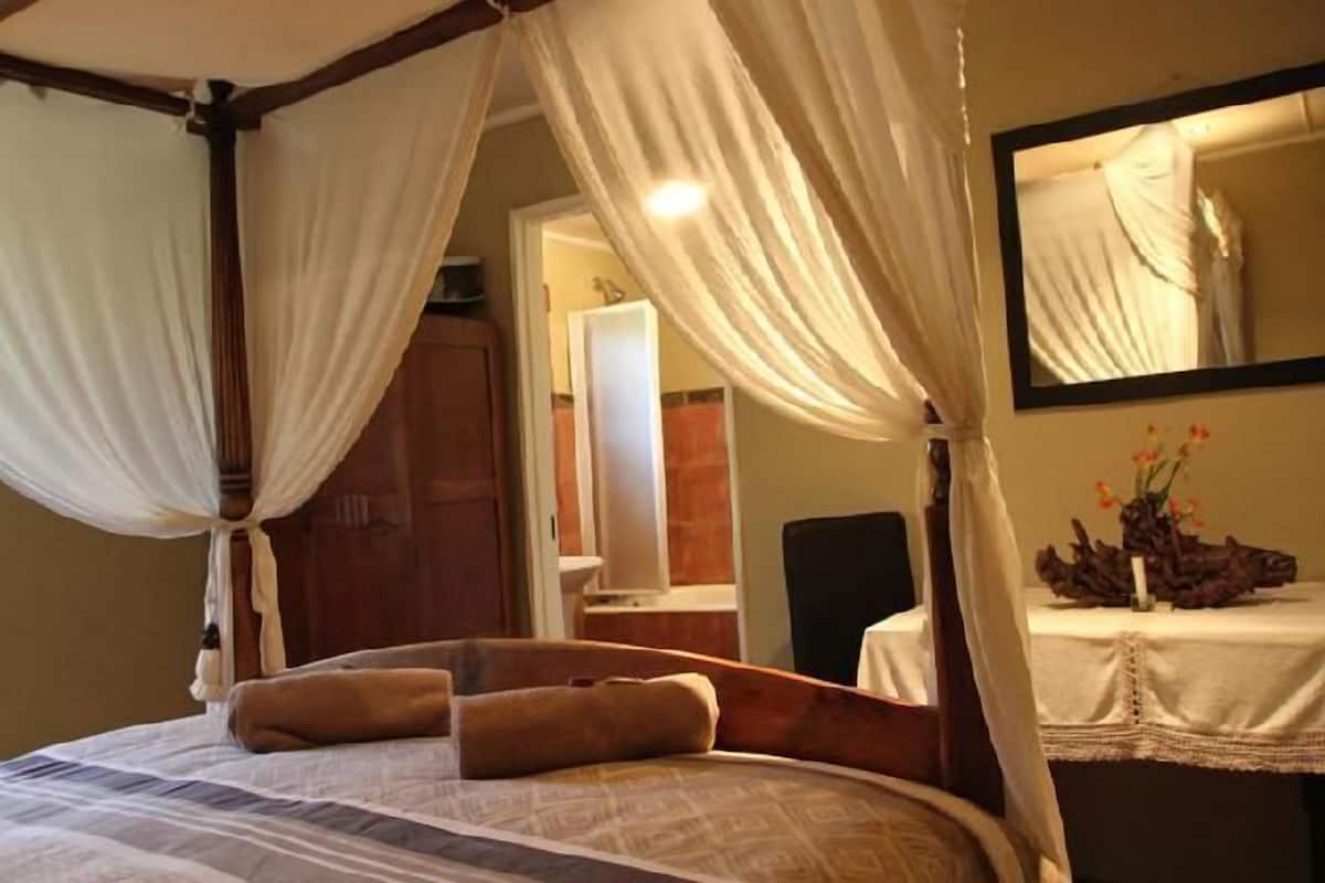 A bedroom with a four-poster bed, a mirror, and a bedside table with a vase of flowers.
