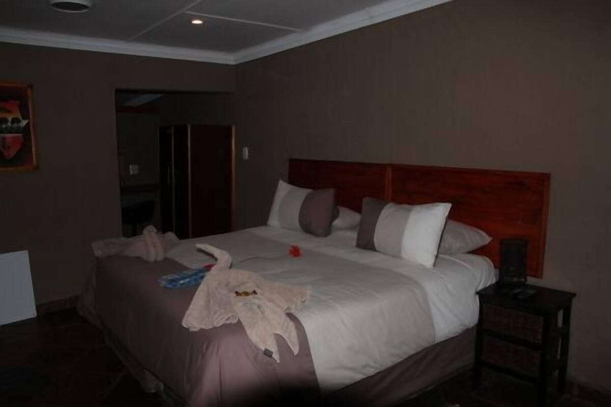 A hotel room with a large bed, a wooden headboard, and a nightstand with a lamp.