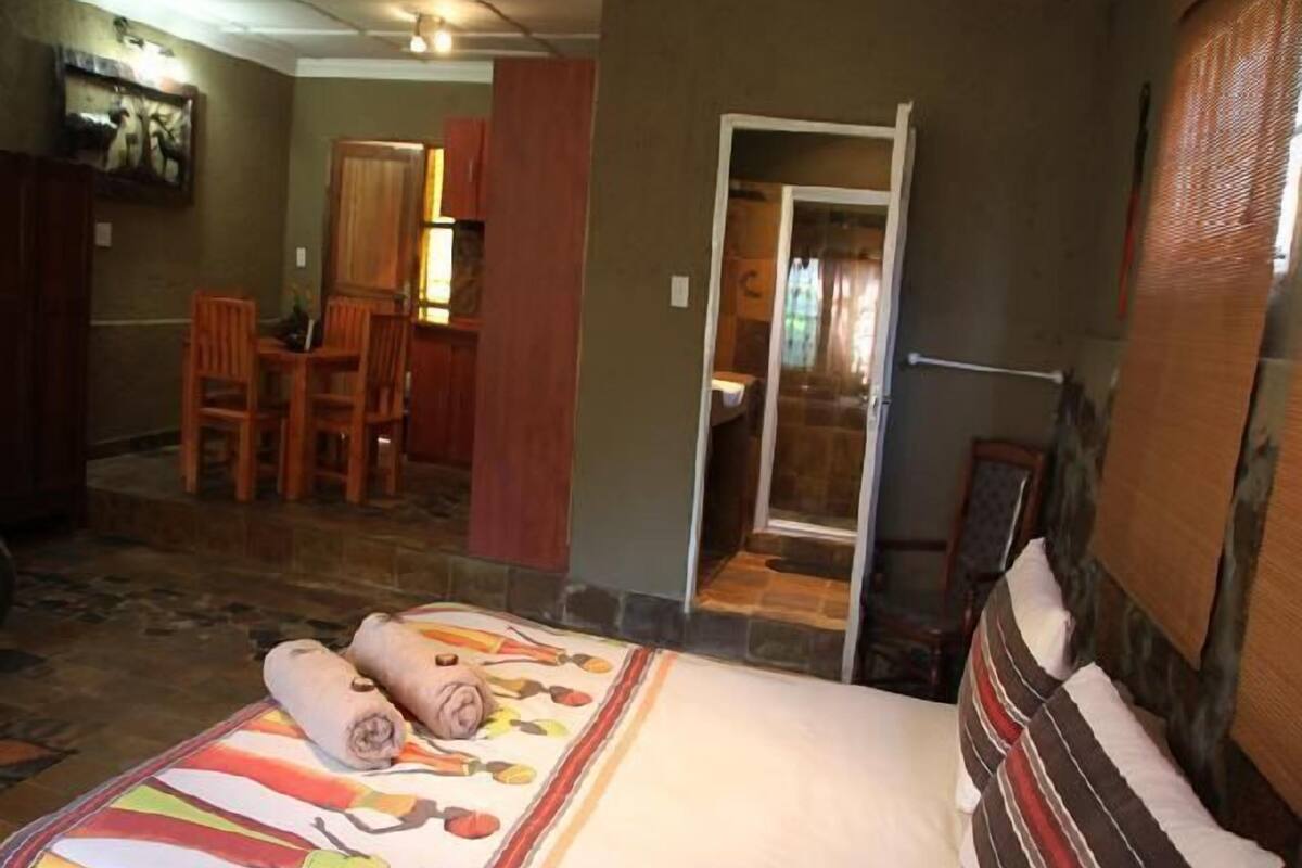 A hotel room with a bed, a desk, and a chair. There is a bathroom visible through an open door.
