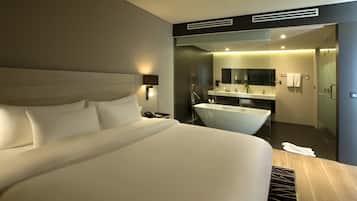A modern hotel room with a large bed, a bathroom with a bathtub, and a mirror above the sink.