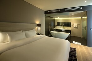 Une chambre d’hôtel moderne avec un grand lit, une salle de bain avec baignoire et un miroir au-dessus du lavabo.