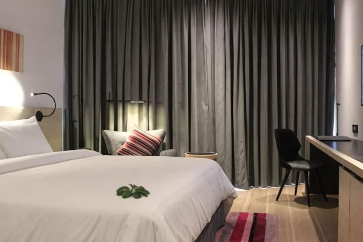 Una habitación de hotel con una cama, un escritorio, una silla, una mesita y una cortina.