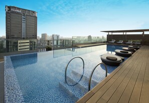 Une piscine à débordement située sur le toit, avec des chaises longues et une vue sur la ville.