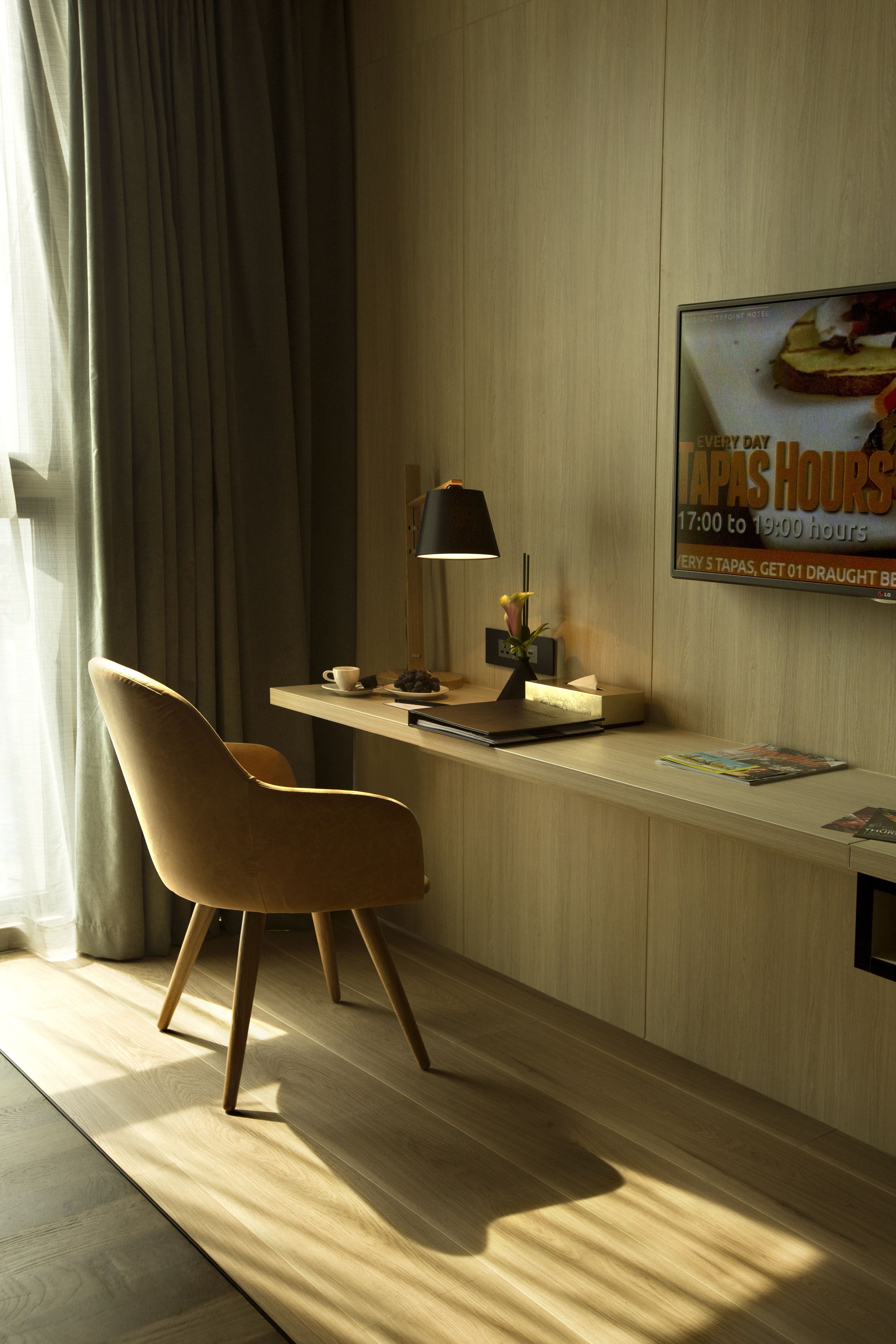 Quarto de hotel moderno com uma escrivaninha de madeira, uma cadeira, um abajur e um cartaz anunciando tapas.