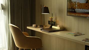 Quarto de hotel moderno com uma escrivaninha de madeira, uma cadeira, um abajur e um cartaz anunciando tapas.