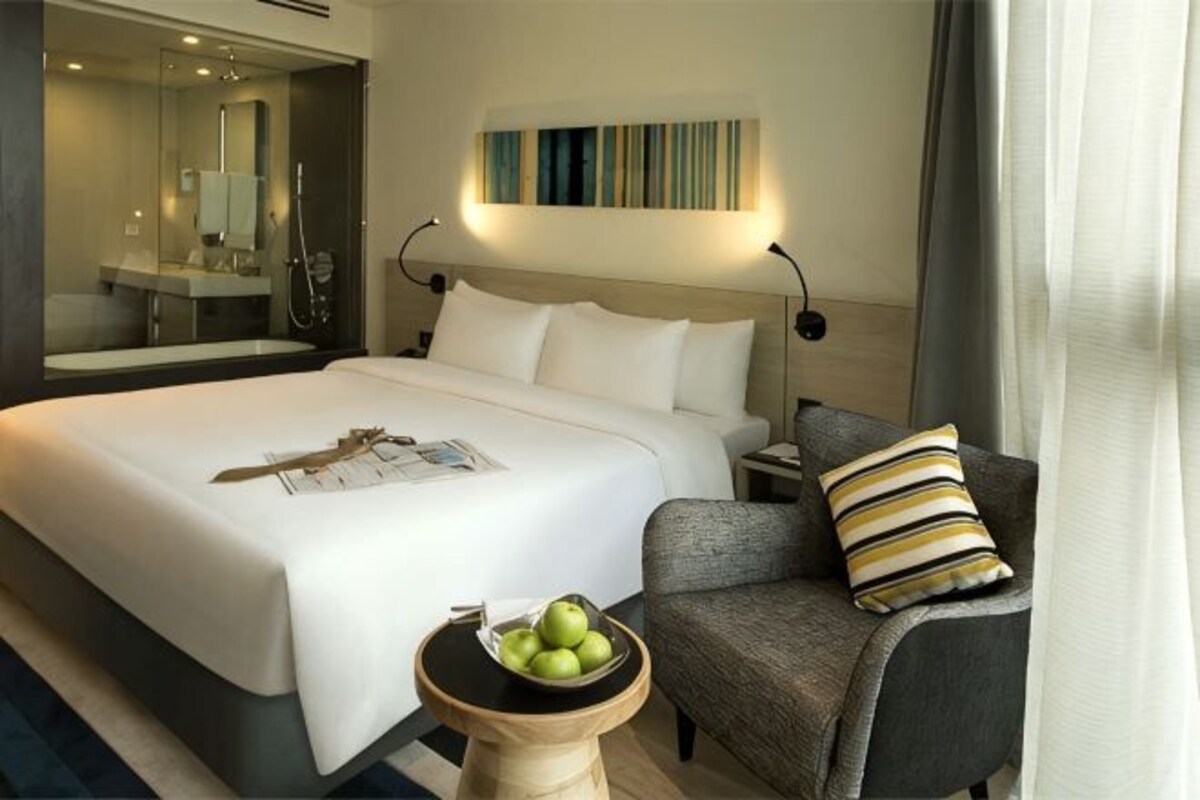 Een hotelkamer met een groot bed, een nachtkastje met een fruitschaal, een stoel en een spiegel.