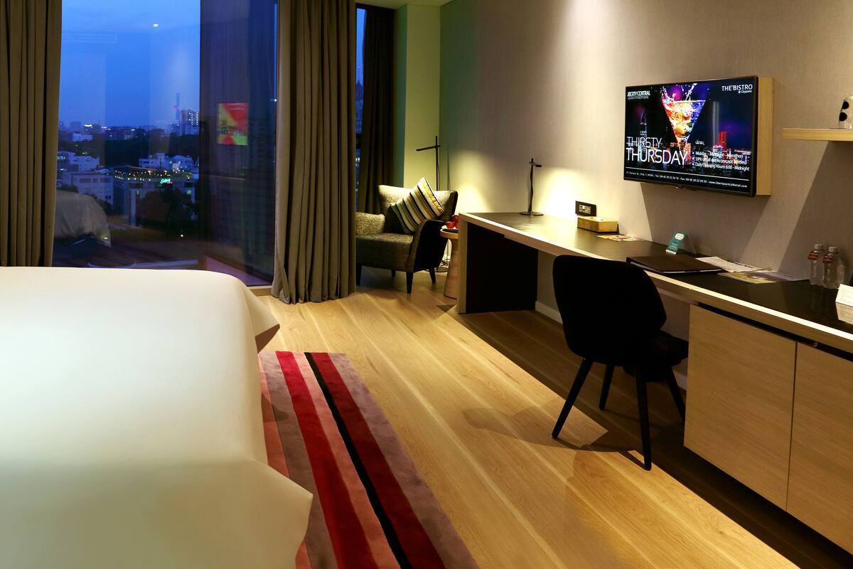 Ein Hotelzimmer mit einem großen Bett, einem Schreibtisch, einem Stuhl, einem Fernseher und Blick auf die Stadt.
