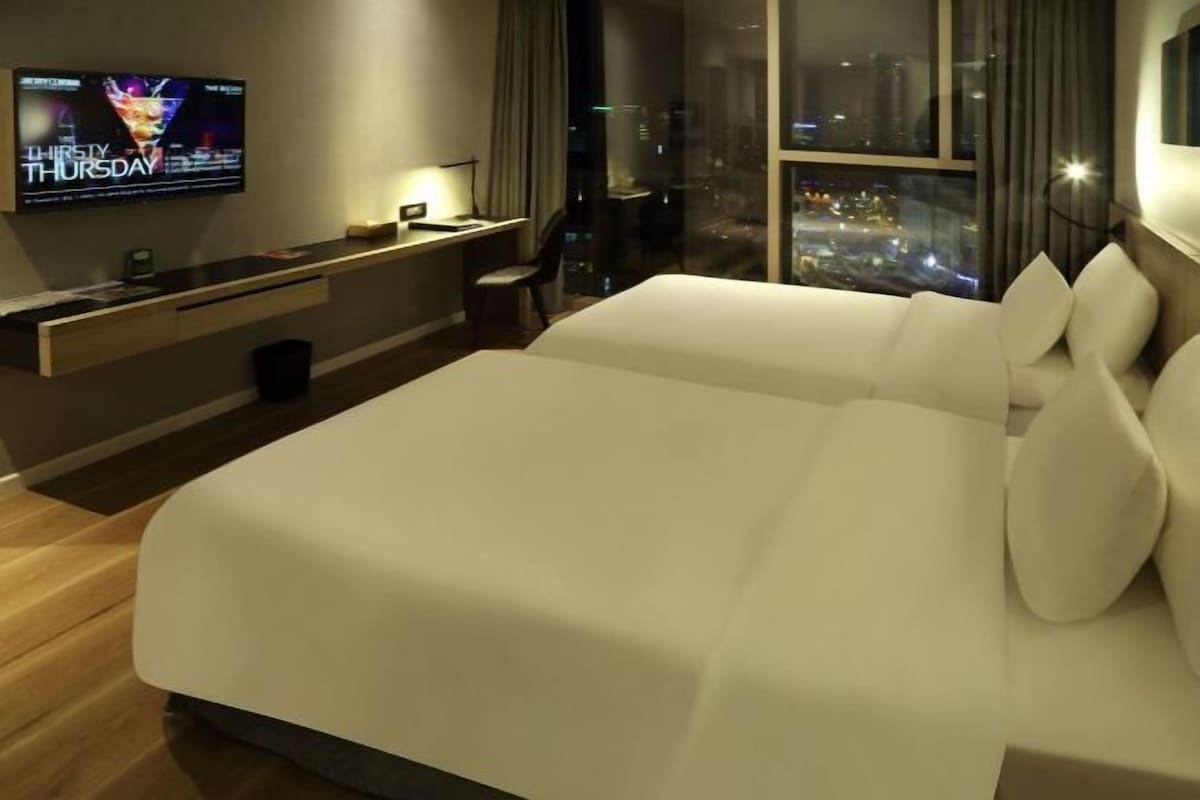 Una habitación de hotel moderna con una cama grande, un televisor en la pared, un escritorio y vistas de la ciudad por la noche.