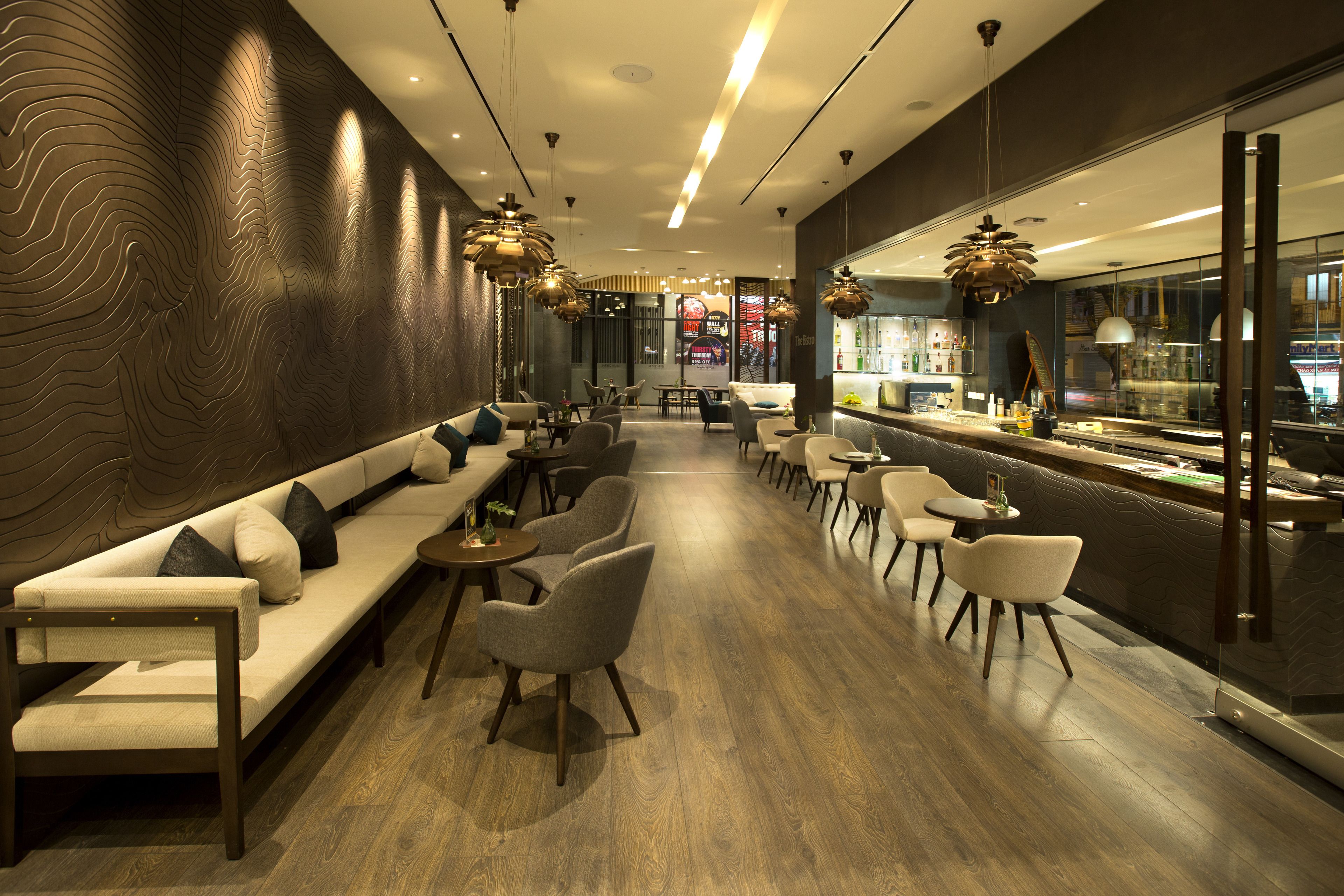 A modern interior with a long sofa, dining tables, and chairs, a bar area, and a patterned wall.