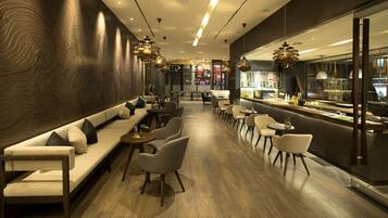 A modern interior with a long sofa, dining tables, and chairs, a bar area, and a patterned wall.