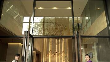 A modern hotel lobby with a glass entrance, a reception desk, and a seating area with a view of the interior.