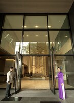 A modern hotel lobby with a glass entrance, a reception desk, and a seating area with a view of the interior.