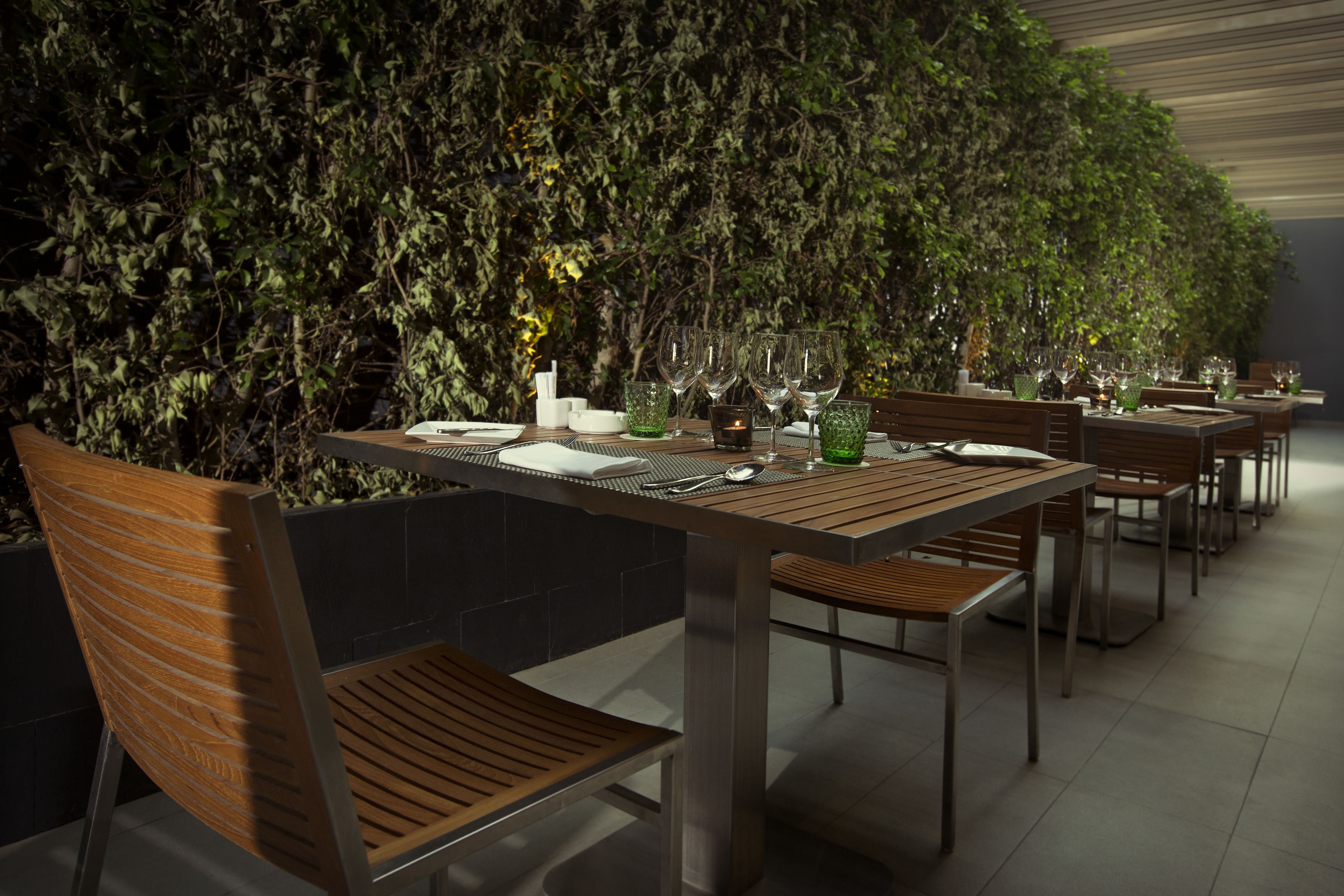 A dining area with wooden tables and chairs, a green plant wall, and a tiled floor.