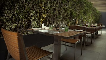 A dining area with wooden tables and chairs, a green plant wall, and a tiled floor.