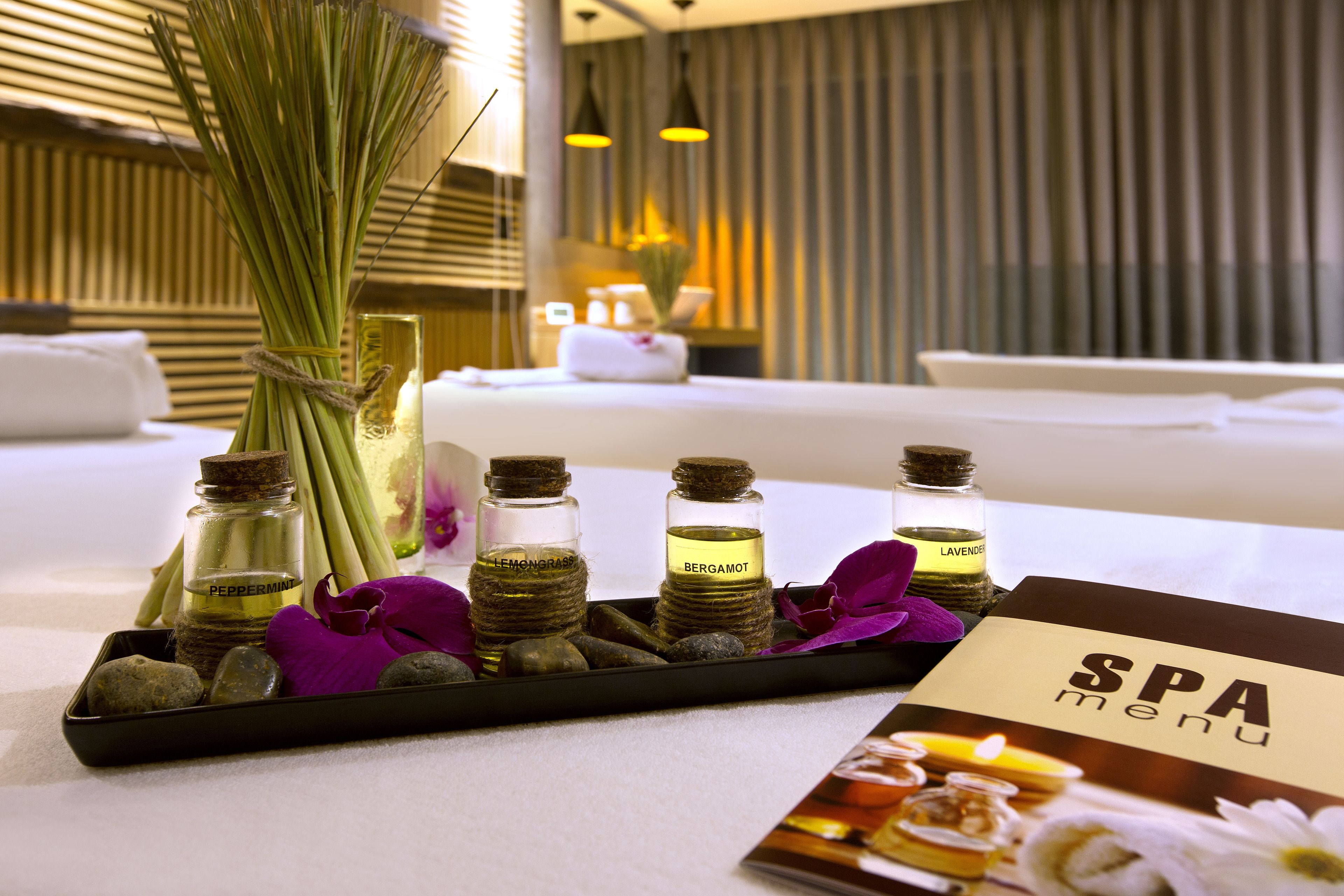 A spa menu on a tray with essential oils, a bouquet of flowers, and a candle.