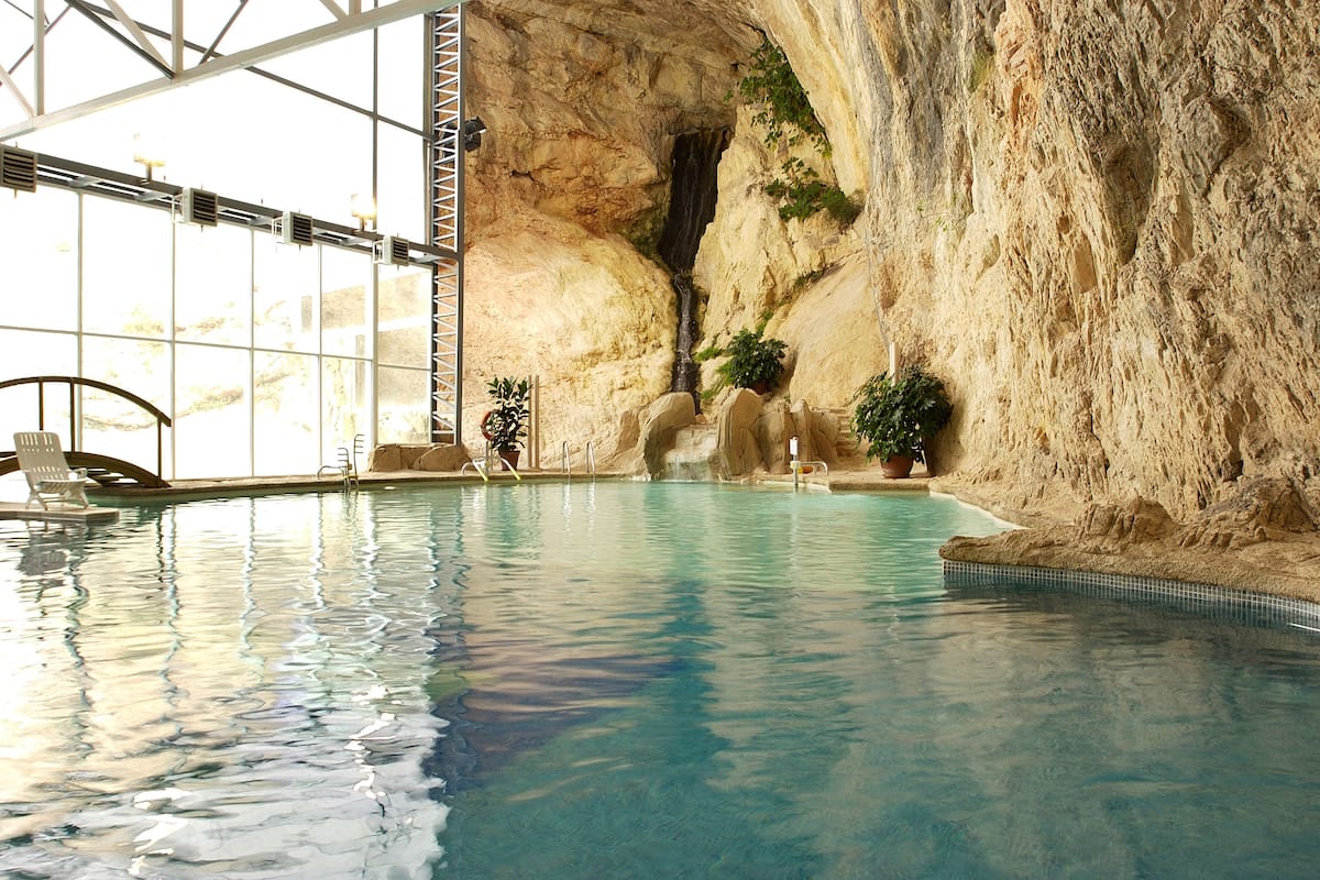 An indoor swimming pool with clear water, a waterfall feature, and large windows allowing natural light.