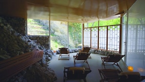 A room with a stone wall, wooden bench, and several wooden chairs. - Balneario Sicilia (Jaraba)