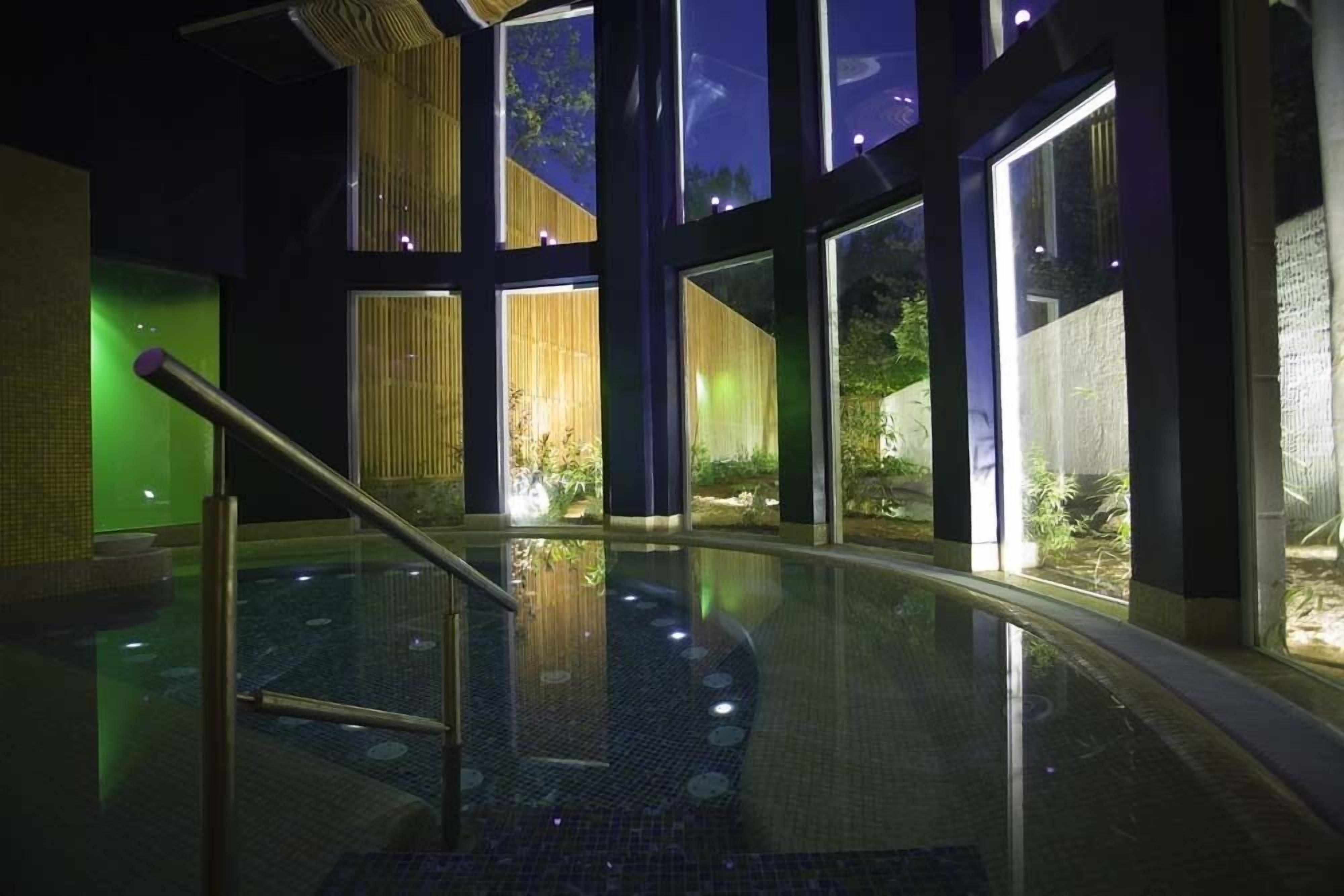 Un área de piscina interior moderna con paredes de vidrio, barandilla de metal y piso de baldosas.