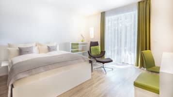 A modern hotel room with a large bed, a desk, a chair, and a window with curtains.