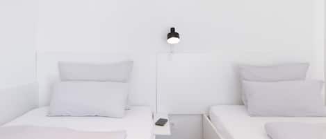 Habitación minimalista con dos camas, una mesita de noche, una lámpara de pared y un enchufe.