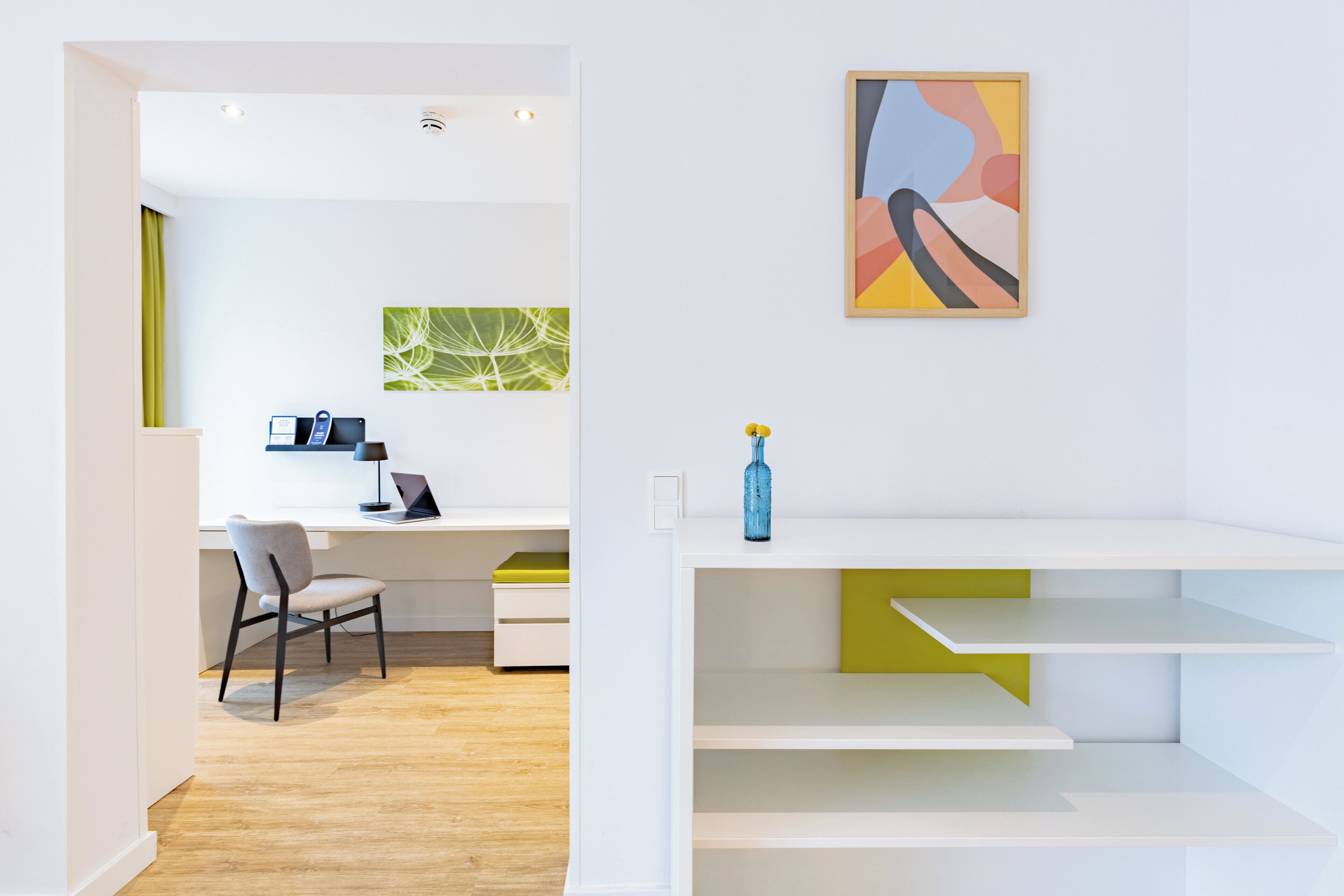 A modern, minimalist room with a desk, chair, and a wall-mounted shelf with a vase.