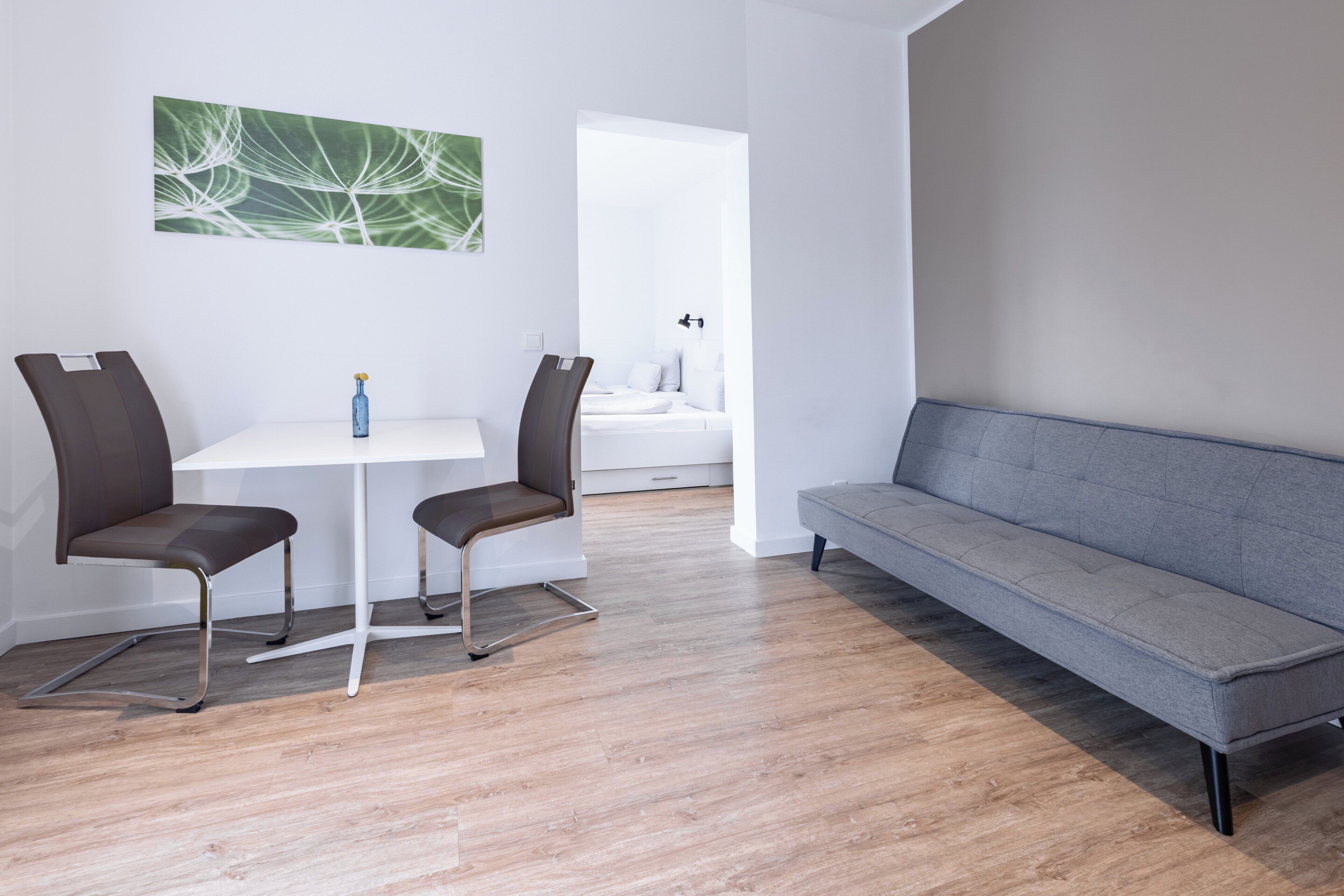 Un salon moderne avec un canapé gris, deux fauteuils marron, une table blanche et un tableau abstrait vert accroché au mur.