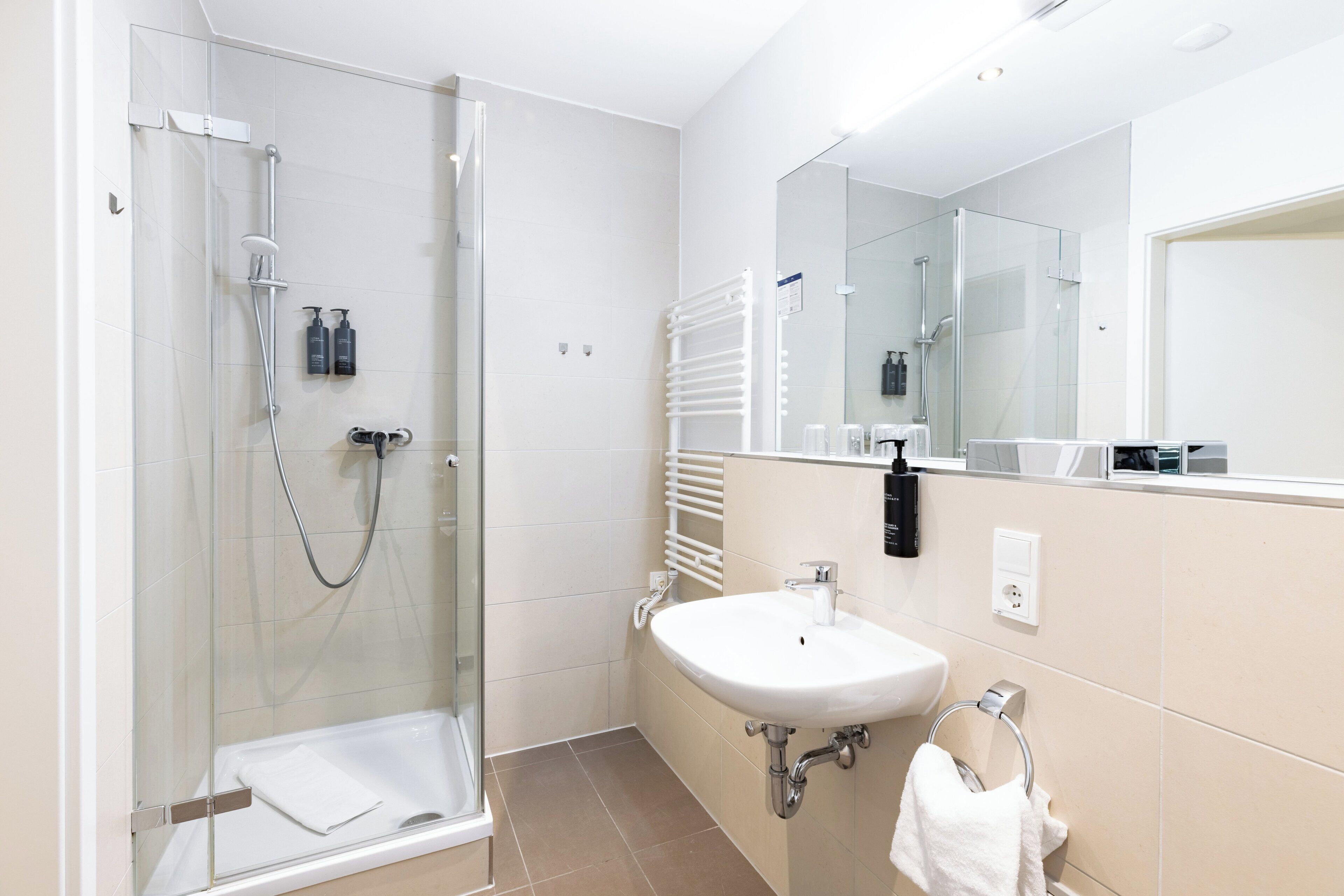 Une salle de bain moderne avec une douche à parois de verre, un lavabo blanc et un grand miroir.