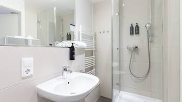Une salle de bain moderne avec un lavabo blanc, une douche en verre et un porte-serviettes.