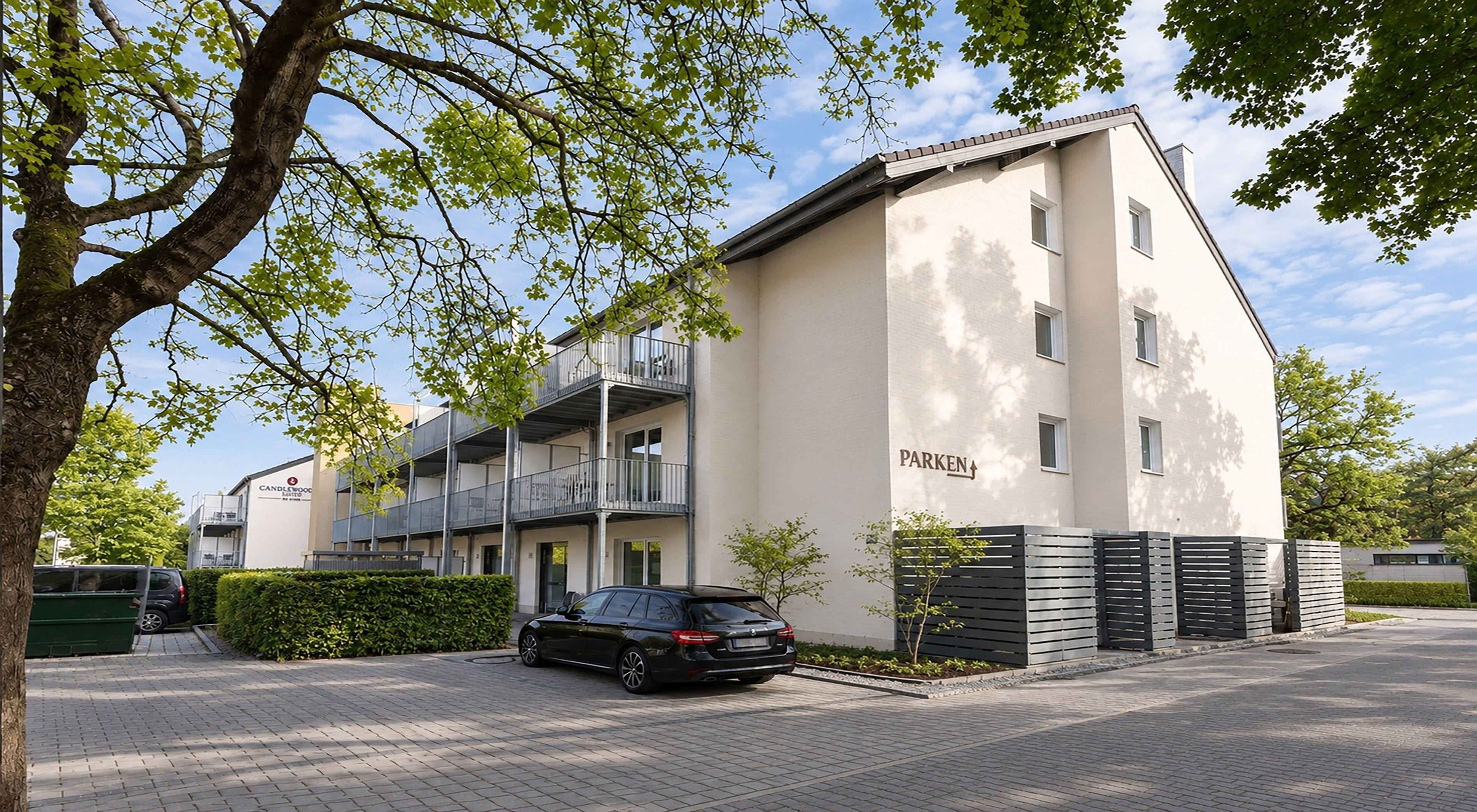 A multi-story residential building with a flat roof, a visible parking area, and a sign indicating the name 'PARKEN'.