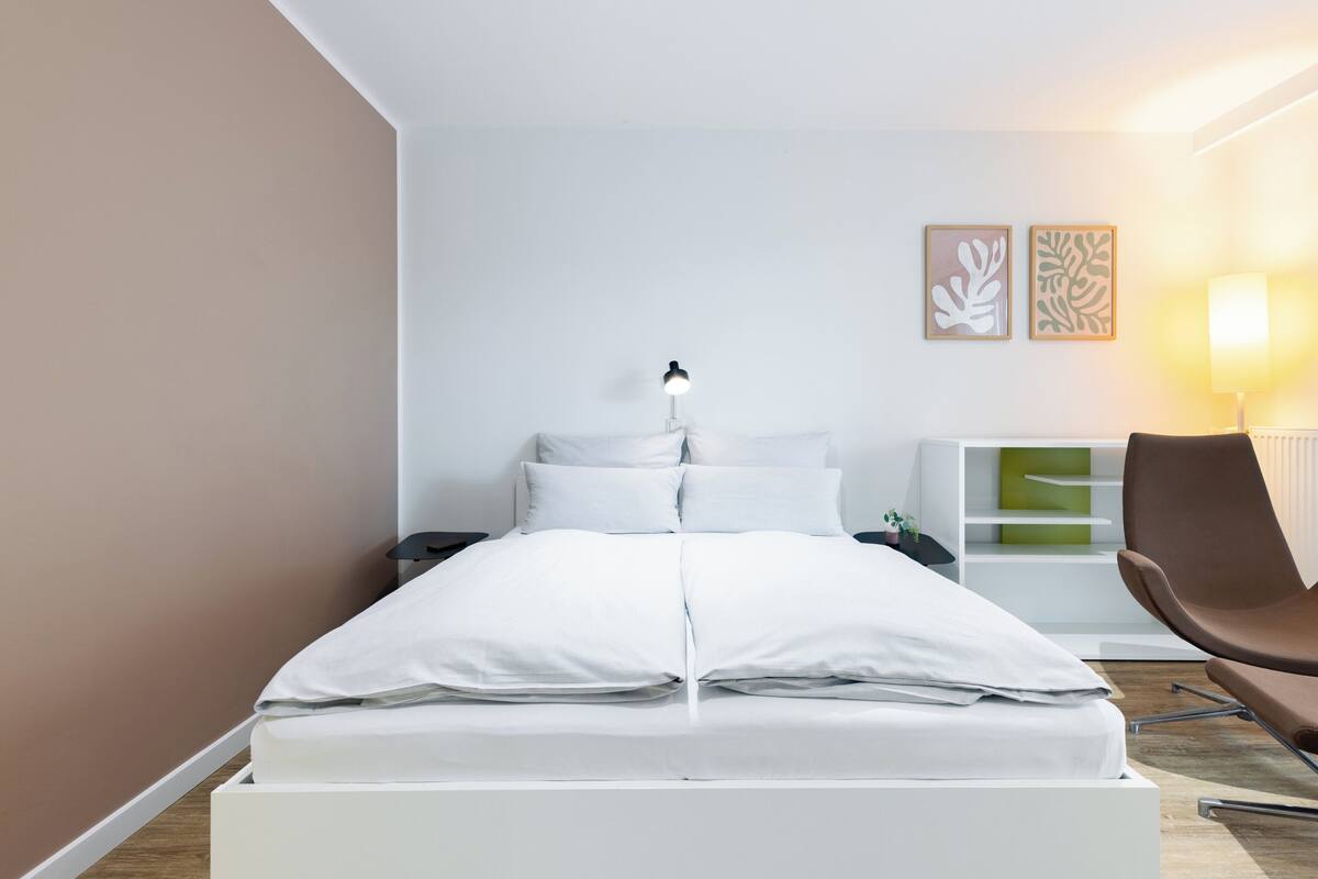 A modern bedroom with a bed, bedside tables, a chair, and wall art.