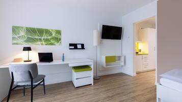 Una habitación de hotel moderna con escritorio, silla, televisor de pantalla plana y una pequeña kitchenette.