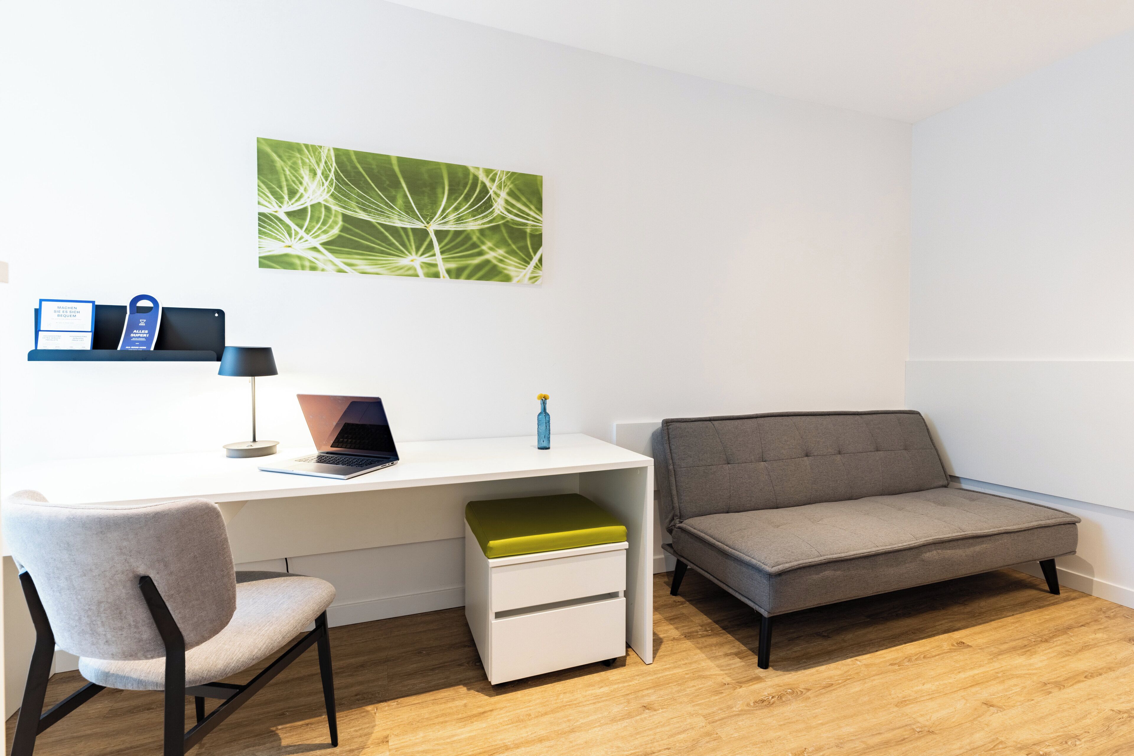 A modern room with a white desk, a grey sofa, a grey chair, and a green cushion.