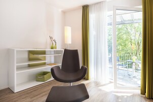 A modern room with a dark armchair, a white shelving unit, and a view of a balcony with outdoor furniture.