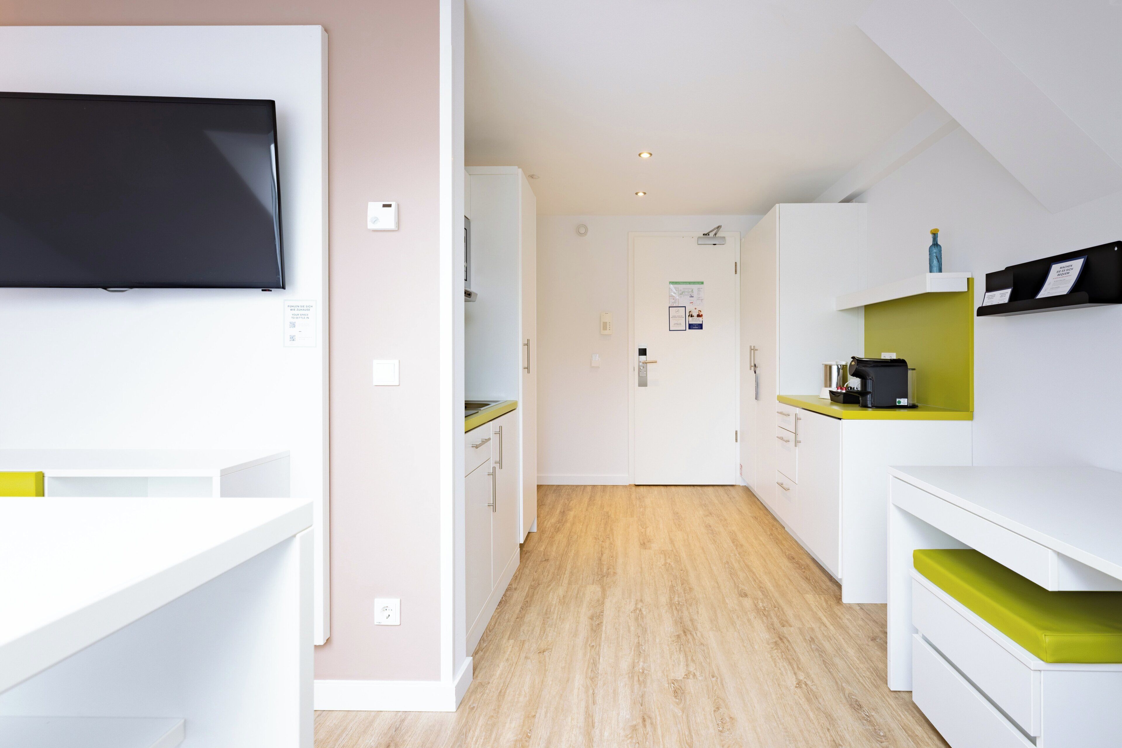 Une cuisine moderne avec des meubles blancs, un téléviseur noir et un plancher en bois.